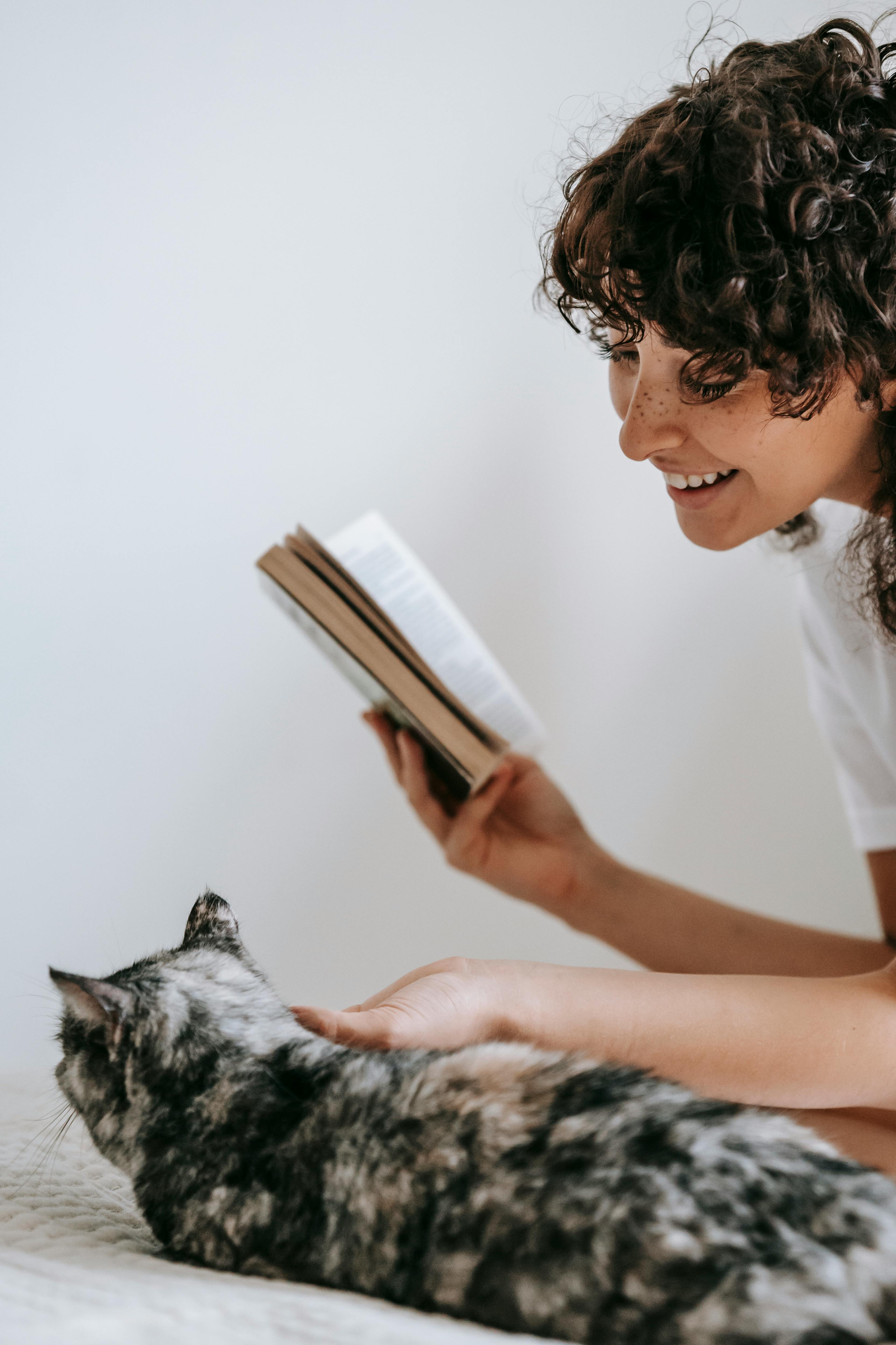 Lady reading in a bed with her cat.